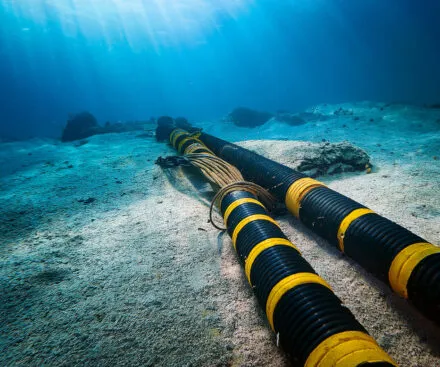an underwater cable badly damaged under water. An underwater view of two thick, black and yellow submarine cables resting on the ocean floor, illuminated by rays of sunlight filtering through the water. These cables, essential for telecommunications and power transmission, stretch into the distance, highlighting the vast infrastructure beneath the sea that supports global connectivity and energy distribution.