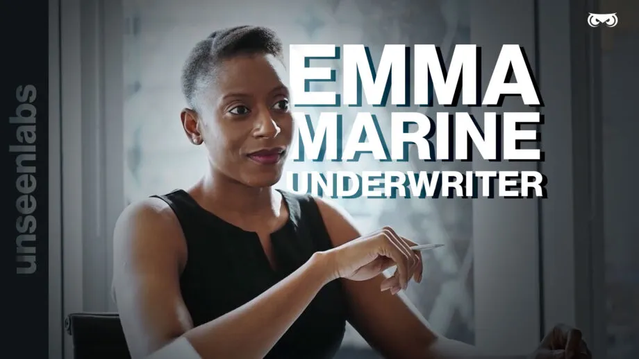 A professional woman with short hair, wearing a black sleeveless top, sits confidently in an office setting with a modern, glass-windowed background. She holds a pen in her right hand, appearing engaged in a conversation. Bold white and blue text overlays the image, introducing her as "EMMA – MARINE UNDERWRITER." On the left side, the Unseenlabs branding is displayed vertically, and a small owl-eye logo is positioned in the top right corner. The image conveys professionalism, expertise, and a focus on maritime underwriting.