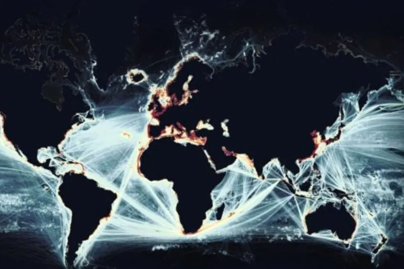 A digital visualization of global maritime traffic, showing a world map with illuminated shipping routes crisscrossing the oceans. The brightest areas, particularly along coastlines and major trade hubs, indicate high-density maritime activity. The glowing white and orange lines contrast sharply against the dark background, emphasizing the vast and interconnected nature of global shipping networks. The image highlights the strategic importance of maritime surveillance and monitoring in ensuring secure and efficient global trade.