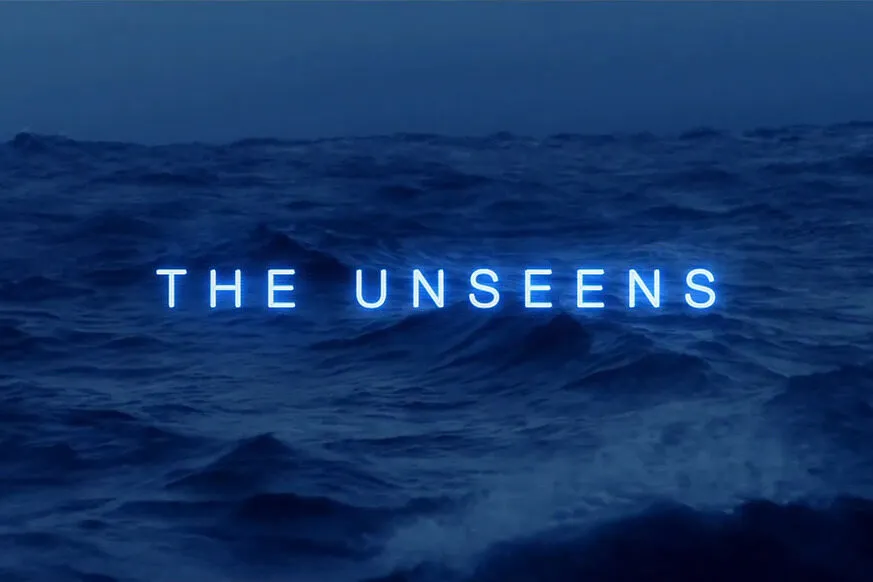 A dark, moody ocean scene with rolling waves under a deep blue sky. In the center, the words "THE UNSEENS" glow in neon blue, creating an eerie and mysterious atmosphere.