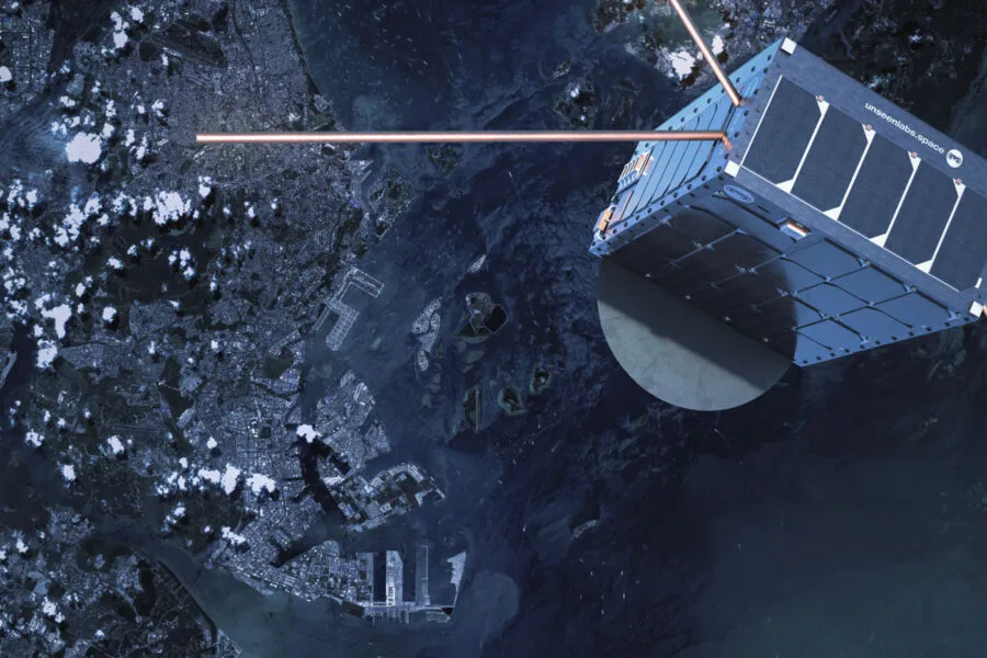 A high-resolution image of an Unseenlabs satellite orbiting Earth, showcasing its cubic design, solar panels, and extended antennas for radio frequency (RF) detection. The satellite is positioned above a coastal city with harbors and waterways visible below, emphasizing its role in maritime surveillance. The satellite's shadow is cast on its metallic surface, while the Earth’s surface, scattered with clouds, provides a striking contrast. This image highlights Unseenlabs’ space-based intelligence capabilities in tracking and monitoring vessels across global waters.
