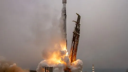 Falcon with BRO-18 inside Launch captured at liftoff, with flames and smoke billowing from the base against a cloudy sky.