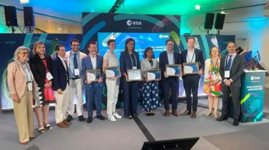 Group photo of award recipients and ESA representatives at the Living Planet Symposium 2025, holding certificates in front of a Copernicus-themed backdrop.