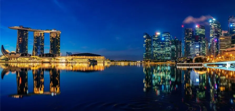Panoramic night view of Marina Bay Sands and the Singapore skyline with brightly lit skyscrapers reflecting on the calm water.